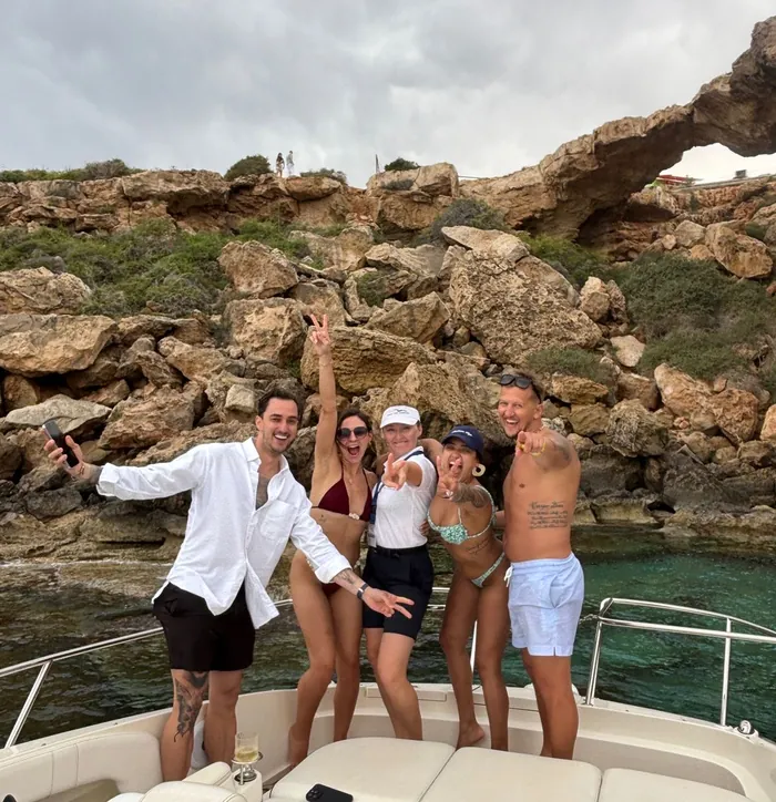 Friends dancing on the bow below the Cape Greco cliffs